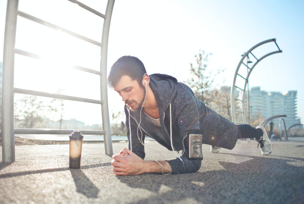 man in an elbow plank, listening to music with headphones next to a bottle of water