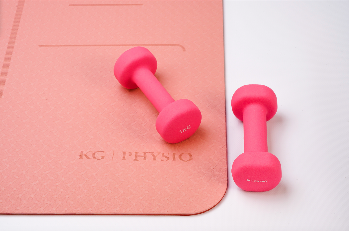 Neoprene-coated dumbbells in bright pink on a yoga mat by KG Physio in salmon pink.